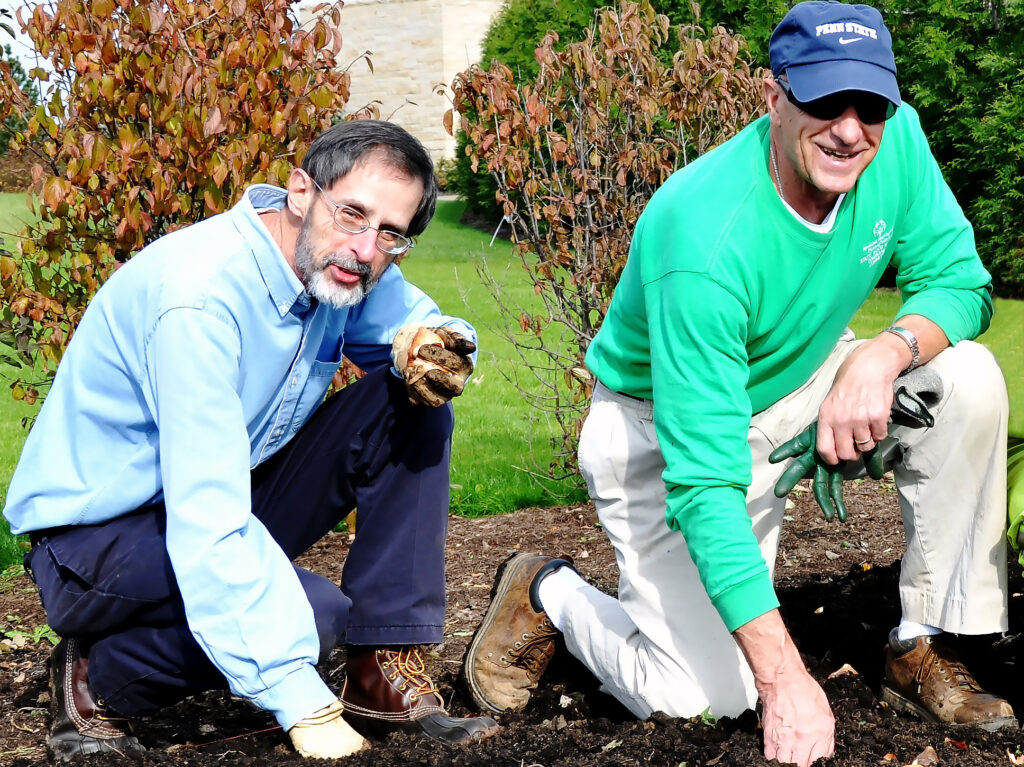 two adult volunteers plant bulbs in soil