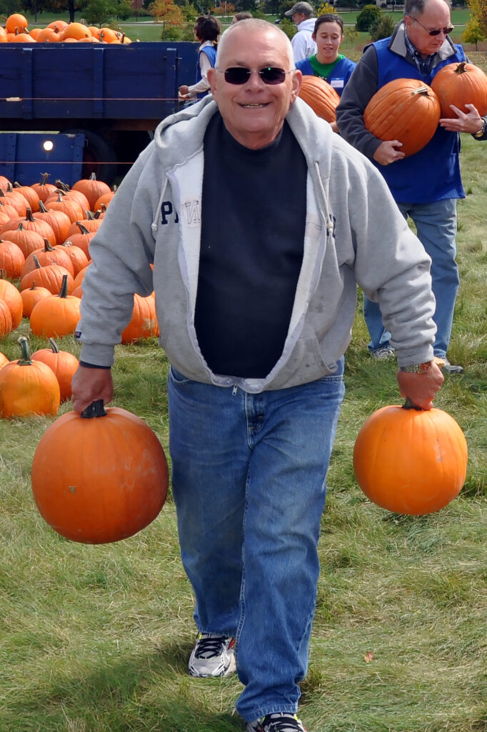 adult volunteer carries two pumpkins