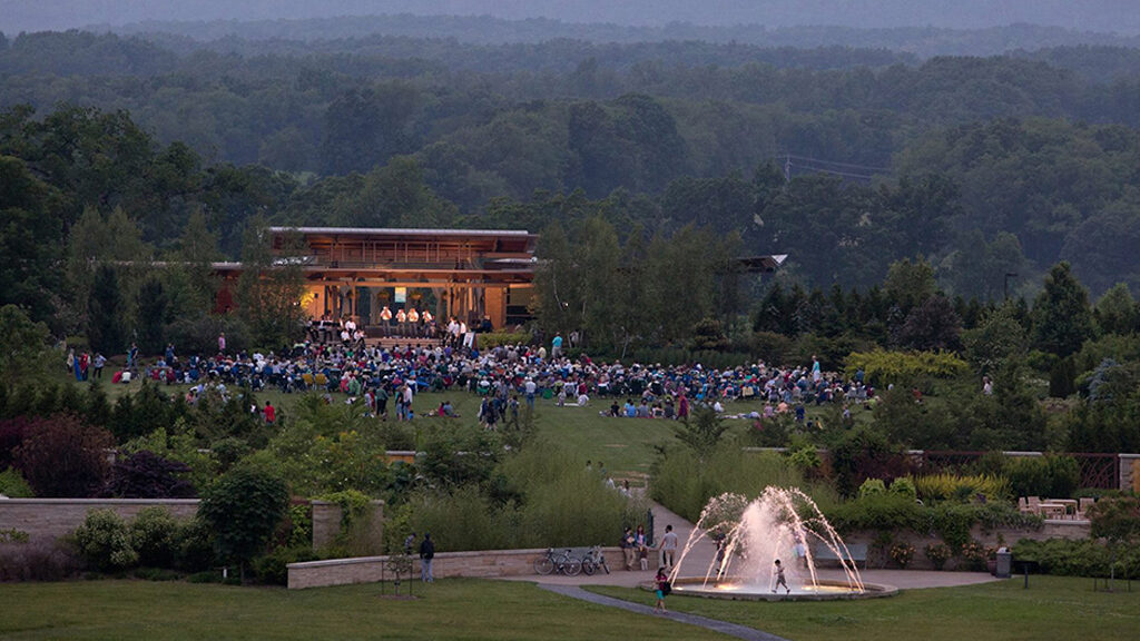 large crowd assembled on the lawn enjoying an outdoor concert at dusk
